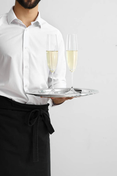 Knappe kelner met glazen champagne op lichte achtergrond - Foto, afbeelding