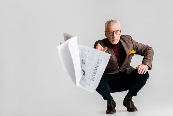 επιλεκτική εστίαση του ώριμος άνδρας ρίχνουν στον αέρα επιχειρηματική εφημερίδα καθμένος σε γκρι - Φωτογραφία, εικόνα