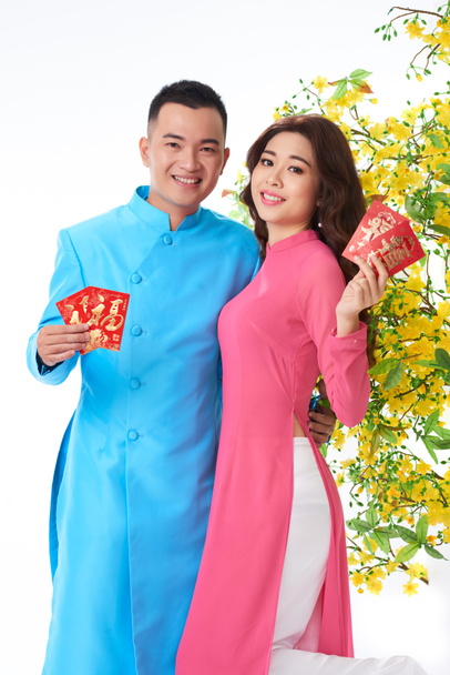 Portrait of cheerful young Asian couple showing cards with best wishes for Lunar year - 写真・画像