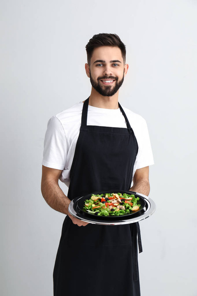 Красивый официант со свежим салатом на светлом фоне
 - Фото, изображение