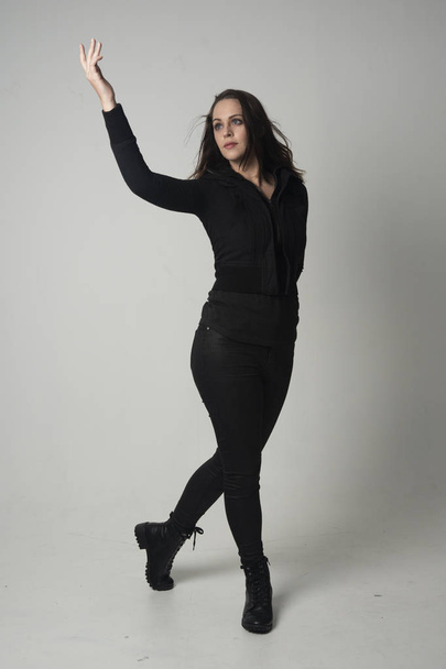 портрет брюнетки в сучасному чорному піджаку і штанях, стоячи позу на сірому студійному фоні
. - Фото, зображення