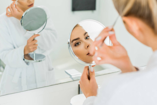 selective focus of beautiful woman plucking eyebrows with tweezers in bathroom  - Photo, Image
