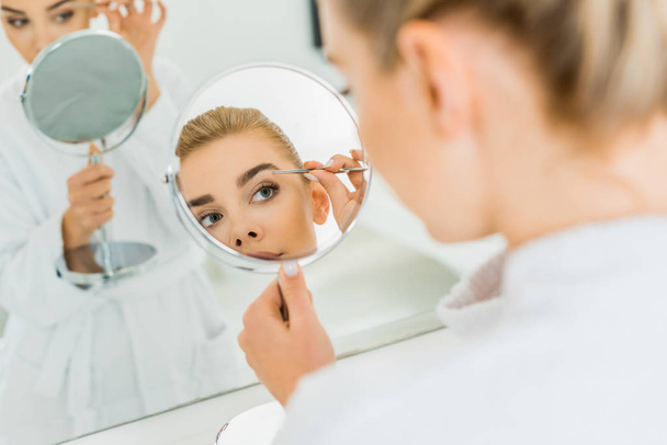 selective focus of attractive woman plucking eyebrows with tweezers in bathroom  - Fotoğraf, Görsel