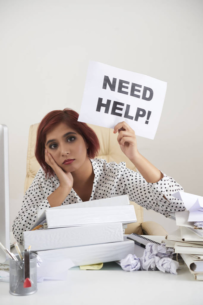 Portret van moe zakenvrouw vraagt hulp tijdens de vergadering op haar werkplek met hoop mappen en documenten - Foto, afbeelding