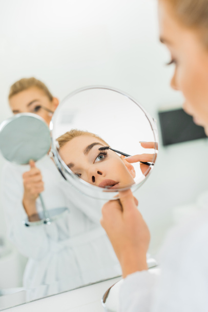魅力的な女性の眉毛をブラッシングと浴室の鏡を見ての選択と集中  - 写真・画像