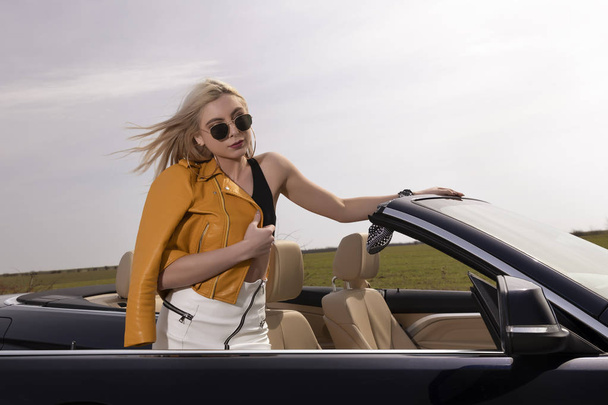 Attraente giovane donna in posa appoggiata su auto convertibile
 - Foto, immagini