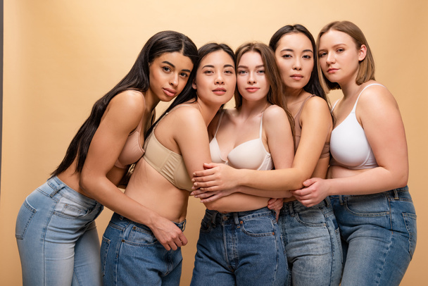 five beautiful multicultural girls hugging and looking at camera isolated on beige, body positivity concept - Photo, Image