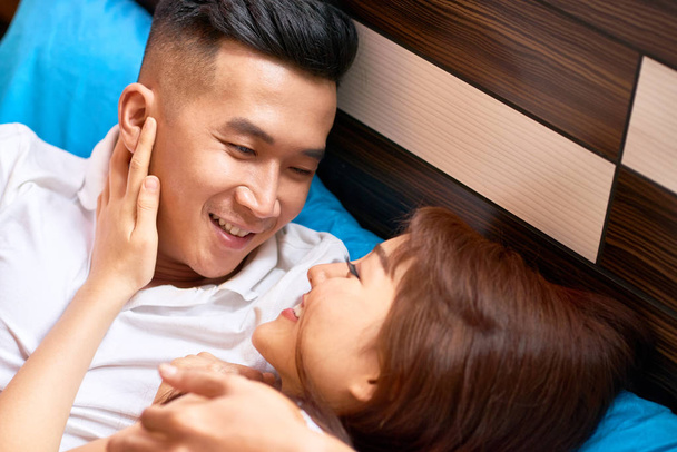 Affectionate Asian young family lying on bed embracing each other and smiling - 写真・画像