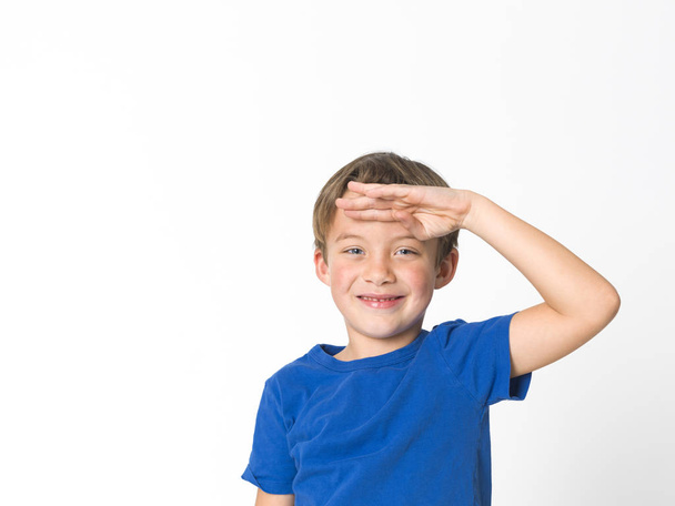 portrait of six year old boy with blue eyes in blue t-shirt holding hand on forehead and looking ahead isolated on white background - Foto, Bild