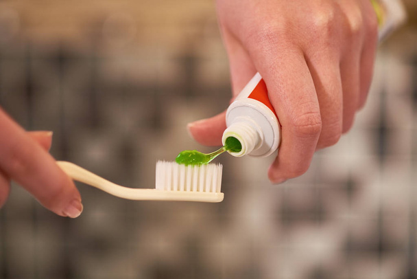 Primer plano de las manos femeninas sosteniendo el cepillo de dientes y aplicando pasta de dientes verde en el baño
 - Foto, Imagen