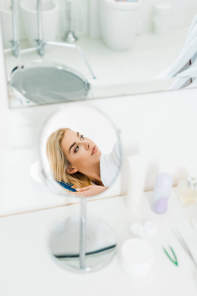 selective focus of beautiful and blonde woman holding comb and looking away in bathroom  - Photo, Image