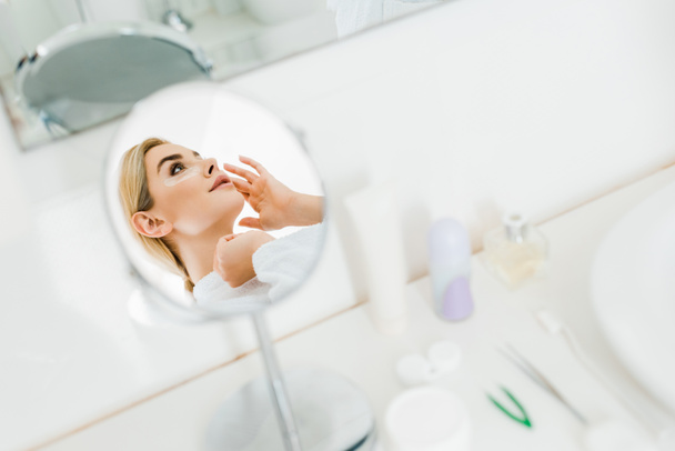foco seletivo de mulher atraente e loira em roupão branco aplicando manchas oculares no banheiro
  - Foto, Imagem