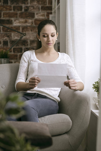 Young woman sitting in the living room and reading a letter - Foto, Imagen