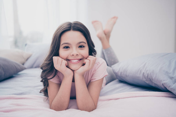 Close up photo cute sweet beautiful she her little girl crossed legs lying down pillow hands arms hold head homey sunday wear home t-shirt pants comfortable apartments flat bright light colored room - Foto, Bild