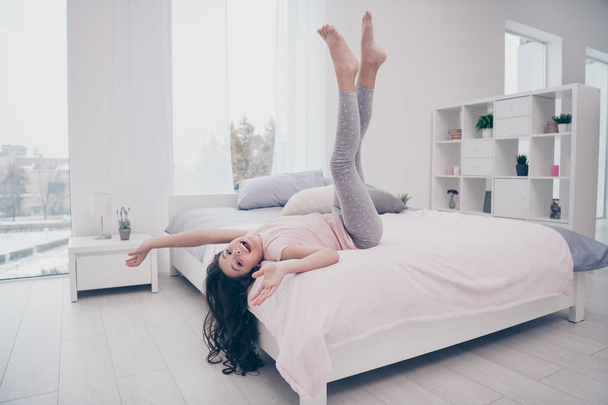 Full length body size side profile photo funky she her little childish girl lying bed upside down curly wavy playful wear home t-shirt pants comfortable apartments bright light colored room indoors - Valokuva, kuva
