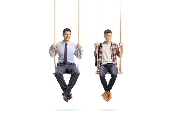 Full length portrait of a teenage male student and a young man sitting on a swing isolated on white background - Photo, Image
