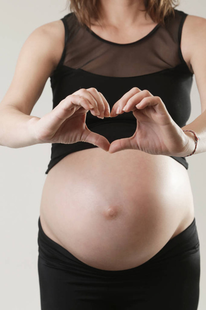 Mujeres embarazadas con las manos en forma de corazón en la barriga
 - Foto, imagen