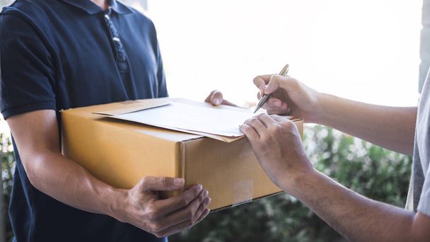 Postbote gibt Paketkasten an Empfänger, junger Mann unterschreibt - Foto, Bild