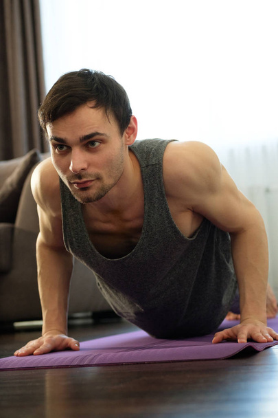 Closeup of a motivated young man doing exercises on an exercise mat at home - Foto, afbeelding