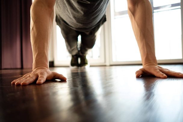 A handsome man doing plank exercises against the window of a house - Photo, image