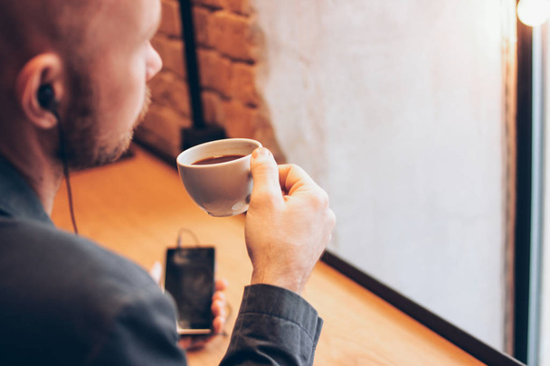Mies, joka käyttää kännykkää ja istuu kahvilassa kahvin kanssa.
 - Valokuva, kuva
