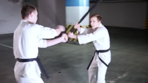 Zwei junge Männer im Kimono trainieren ihre Fertigkeiten auf einer Tiefgarage. Schwertkampf - Filmmaterial, Video