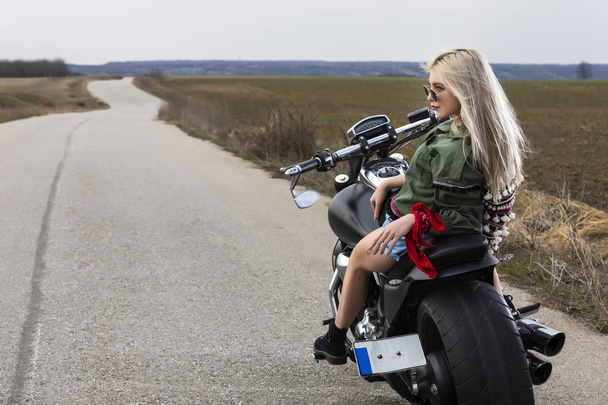 eine schöne junge Frau sitzt auf einem schwarzen und chromfarbenen Motorrad - Foto, Bild