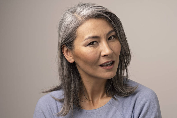 Pensive Adult Woman of Mongolian Nationality with Gray Hair on a Gray Background. - Foto, Bild