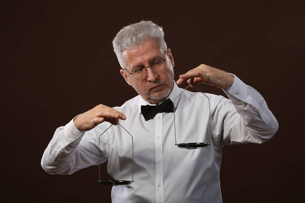Uomo anziano dai capelli grigi anni '50, in camicia bianca, occhiali e papillon del peso di qualcosa su bilance con kettlebells
 - Foto, immagini