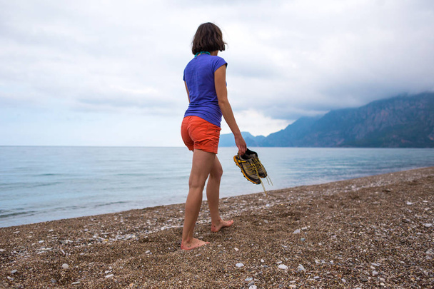 Barefoot brunette on the background of the ocean and overcast sky. - Photo, Image