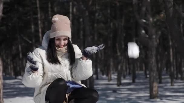 Een mooi meisje in een pine park geniet besneeuwde winterweer, ze gooit speels omhoog een armful sneeuw over haar hoofd, die prachtig kruimels en verandert in kleine sneeuwvlokken - Video