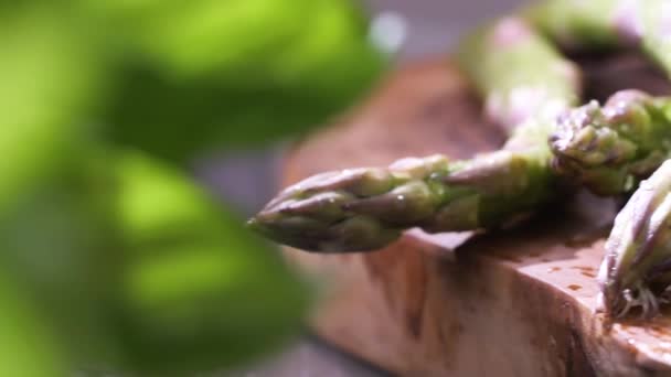 close-up view of fresh wet green asparagus with salt on wooden board, selective focus  - Imágenes, Vídeo