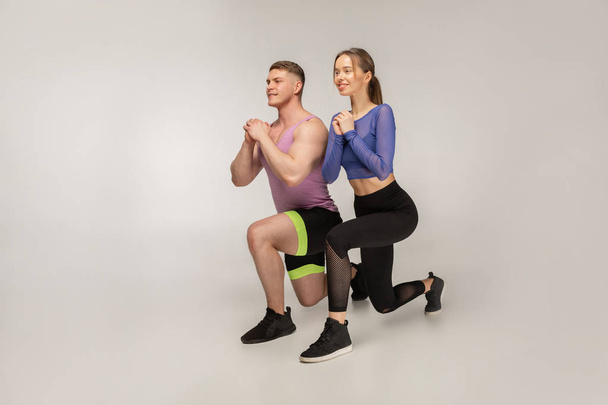 Sporty young couple in trendy colorful sportswear doing lunge on left foot - Φωτογραφία, εικόνα