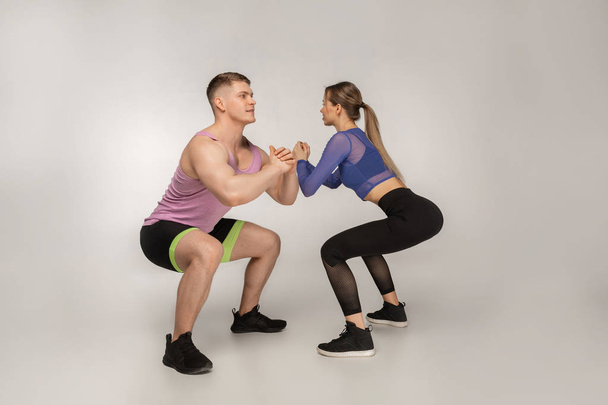 Young attractive couple in trendy sportswear doing sguats together - Foto, afbeelding