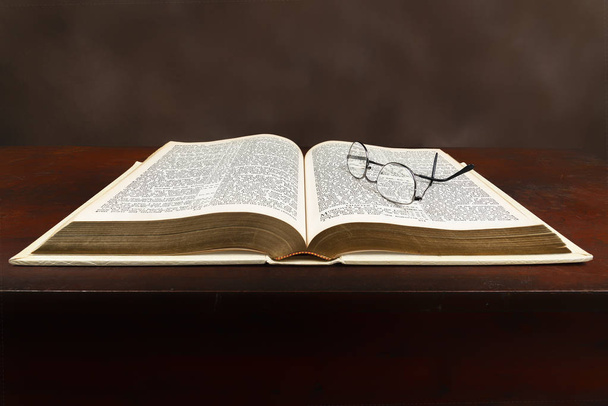 Bíblia velha na área de trabalho velha com óculos
 - Foto, Imagem