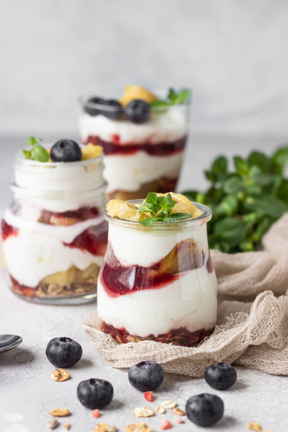 Granola, blueberry and banana greek yogurt parfaits in mason jars. Healthy breakfast. A light grey concrete background. Copy space. - Foto, immagini