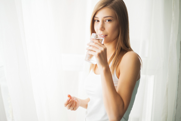 Conceito de saúde. Jovem mulher segurando pílula e copo de água
 - Foto, Imagem