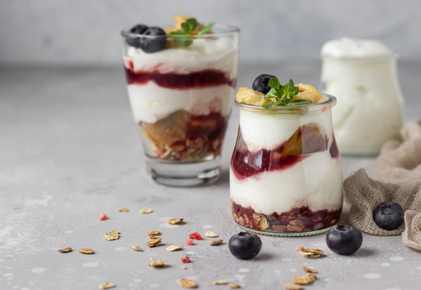 Granola, blueberry and banana greek yogurt parfaits in mason jars. Healthy breakfast. A light grey concrete background. Copy space. - Φωτογραφία, εικόνα
