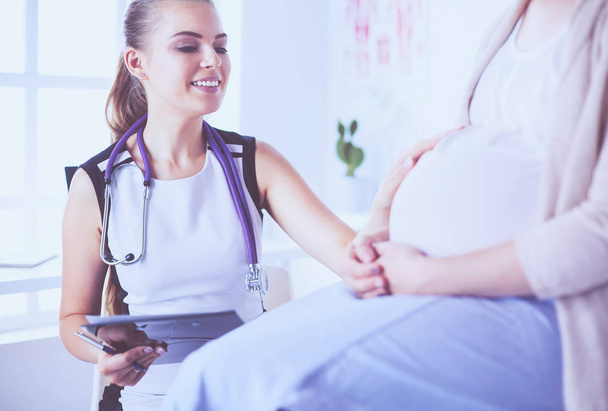 Fiatal nő orvos sztetoszkóppal és tablettával beszél terhes nővel a kórházban. - Fotó, kép