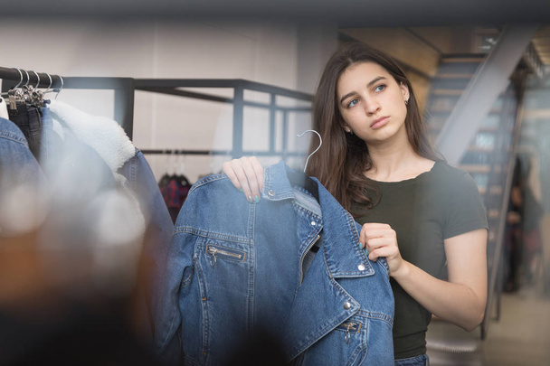 The girl in the clothing store chooses a denim jacket, chose and pressed to her. - Photo, Image