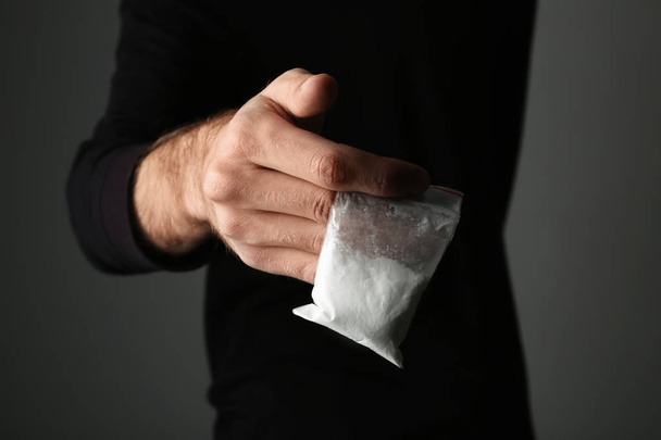 Drug dealer holding bag with cocaine on dark background, closeup - Photo, image