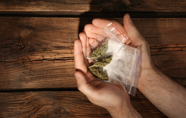 Man holding plastic bags with cocaine and hemp buds on wooden background, top view. Space for text - Photo, Image