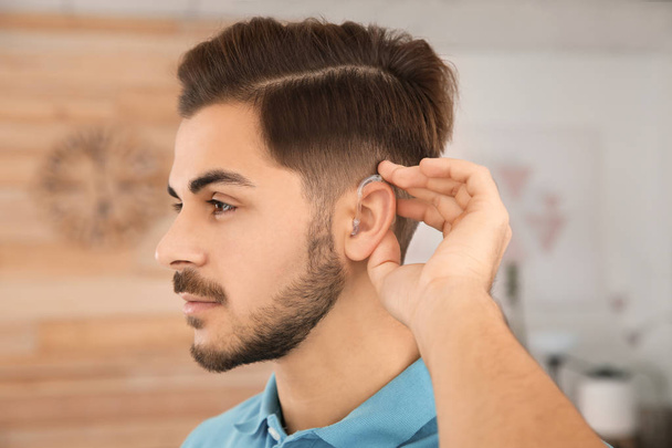 Young man adjusting hearing aid at home - Foto, Imagem