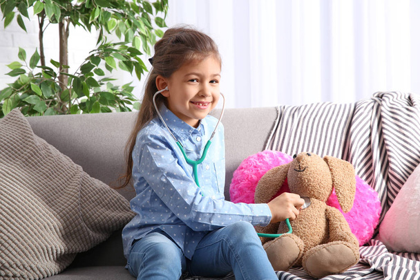 Cute child imagining herself doctor while playing with stethoscope on sofa in living room - Photo, image
