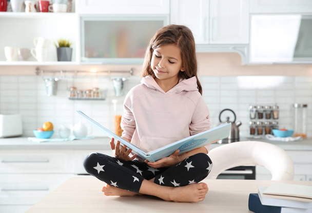 Cute little girl reading book in kitchen at home - Photo, Image