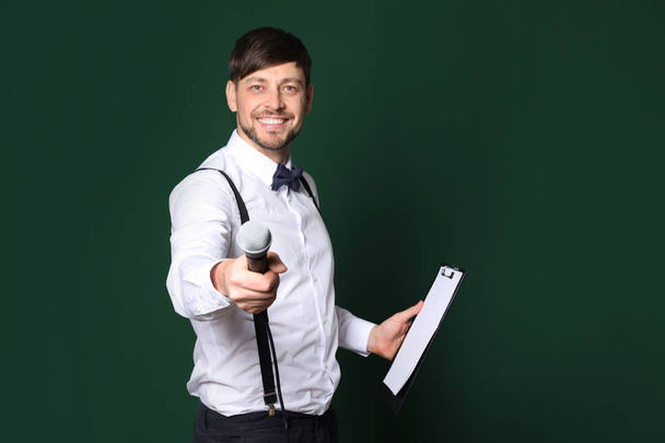 Handsome man in formal clothes with microphone and clipboard on color background. Space for text - Foto, afbeelding