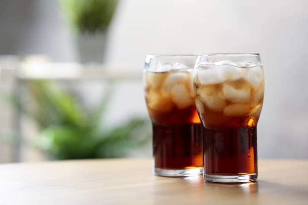 Glasses of cola with ice on table against blurred background, space for text - Photo, image