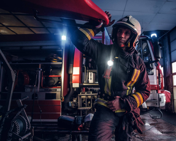 Ένας πυροσβέστης που φοράει μια προστατευτική στολή με φακό περιέλαβε την εργασία σε ένα πυροσβεστικό σταθμό γκαράζ - Φωτογραφία, εικόνα