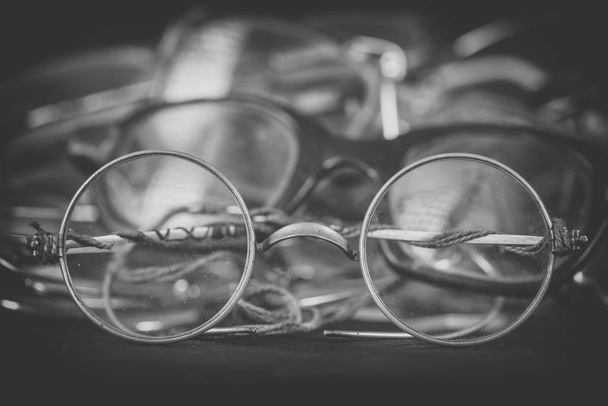 Espectáculos retro redondos de cerca, efecto monocromo. Montón de gafas rayadas y rotas. Reparación y sustitución de anteojos viejos, cuidado de los ojos
 - Foto, imagen