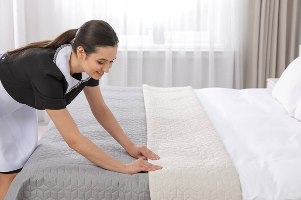 Young maid making bed in hotel room - Foto, Imagem